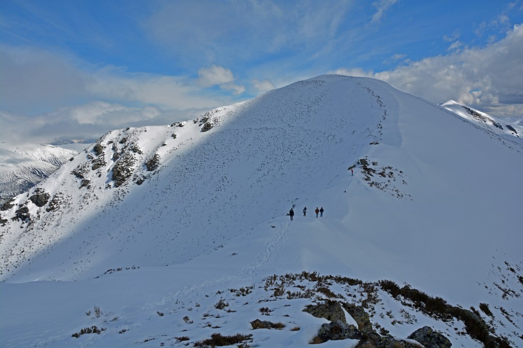 Caminando por la cresta nevada de una montaña cerca del Puerto de Ancares, puerto de montaña de la sierra de Ancares que une la provincia de Lugo, con la provincia de León, a través de su municipio de Valle de Ancares, Ancares, El Bierzo, León, Castilla y León, España.