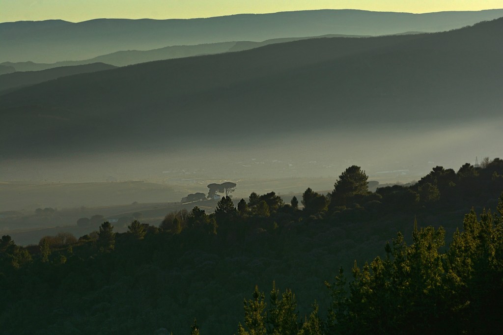 La silueta de la Casilla de los Pinos se perfila en el horizonte con el fondo de las montañas cubiertas de niebla en una toma desde una cota elevada cercana a Valtuille de Arriba, Villafranca del Bierzo, El Bierzo, León, Castilla y León, España.